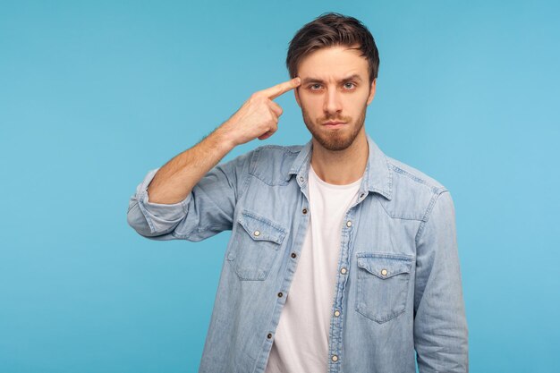 Idea loca Retrato de hombre en camisa de mezclilla mostrando un gesto estúpido mirando a la cámara con condena y culpando por plan loco sugerencia tonta tiro de estudio interior aislado sobre fondo azul