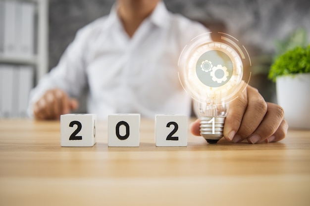 Foto idea y planificación empresarial en el concepto 2021, empresario sosteniendo la bombilla del plan de innovación con un cubo de número en la mesa de madera