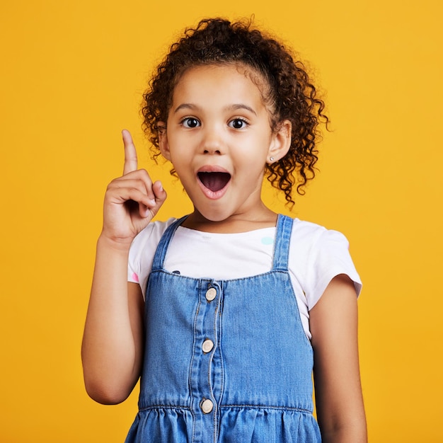 Idea sorpresa y retrato de una niña señalando aislada en un fondo de estudio amarillo con conocimiento del plan de choque y niño pequeño feliz con ideas brillantes y planificación inteligente haciendo gestos al espacio