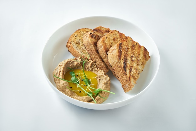 Ideale Vorspeise - Putenleberpastete mit Mangosauce und Roggenbrot in einem weißen Teller auf weißem Hintergrund