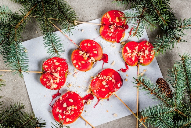 Ideas de invierno, dulces navideños. Dulces para niños. Rodajas de manzana de chocolate en caramelo rojo y nueces. Fondo de piedra gris, con ramas de árboles de Navidad, vista superior