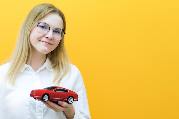 Idee und Konzept der Fahrschule Schülerfahrer hat die Prüfung bestanden Führerschein Porträt einer schönen glücklichen jungen Frau, die ein Auto in der Hand auf gelbem Hintergrund hält und das Auto anschaut