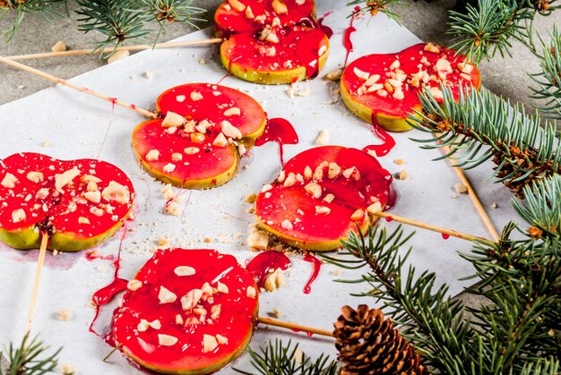 Ideen des Winters, Weihnachtsleckereien. Süßigkeiten für Kinder. Schokoladen-Apfelscheiben in rotem Karamell und Nüssen. Grauer Steinhintergrund, mit Weihnachtsbaumasten, Draufsichtkopienraum