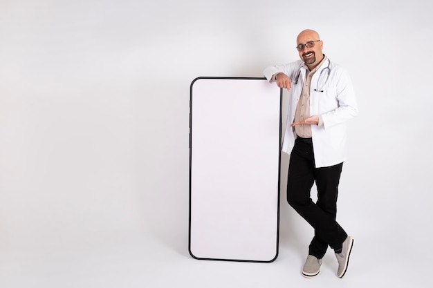 Idéia do conceito médico, médico masculino caucasiano, inclinando-se para grande smartphone com tela em branco para simular.