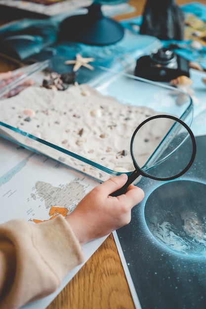 Foto ideia para uma atividade com uma criança com areia e conchas aprendendo geografia