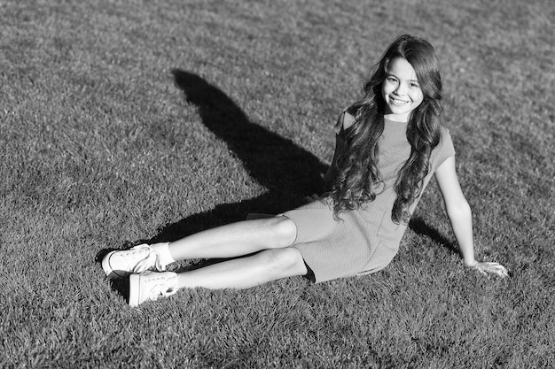 Idéias de férias Garota sorridente feliz, relaxe no gramado Estudante alegre Divirta-se Garota fofa sente-se na grama verde Garota feliz emocional relaxando ao ar livre O que faz a criança feliz Férias de verão