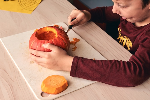 Idéias de halloween, decoração e feriados - close up de criança com abóbora escultura de faca ou jack-o-lantern. menino de 6 anos tem atividades divertidas em família. mãe passando um tempo com filho juntos