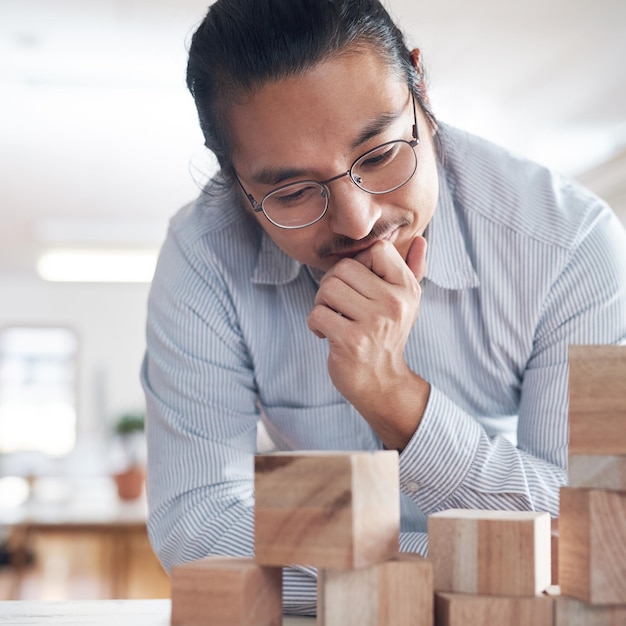 Foto idéias de pensamento e homem asiático no escritório com jogo de estratégia de blocos de construção e equilíbrio de design com inovação arquitetura de engenharia e designer com jogo de bloco de madeira de ideia e resolução de problemas