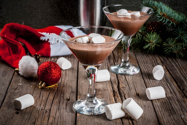 Ideias para bebidas de festa de Natal, coquetéis caseiros de Martini de Chocolate Quente com marshmallow, na velha mesa de madeira rústica com decorações de Natal, copie o espaço