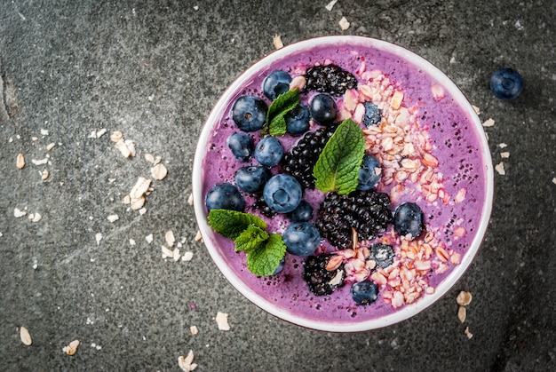 Idéias para café da manhã saudável verão. Batido na tigela com baga azul (mirtilo) Com aveia, frutas frescas. Mesa de pedra escura. Espaço de cópia da vista superior