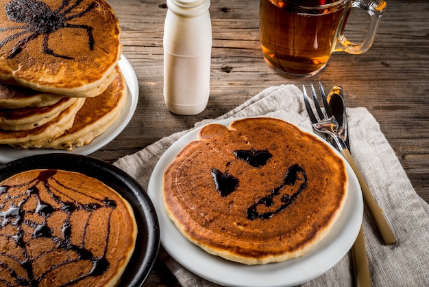 Idéias para o café da manhã são Halloween, comida para crianças. Panquecas de torta de abóbora decoradas com calda de chocolate em um estilo tradicional - teia de aranha, aranha, lanterna de jack. Na mesa rústica de madeira, copie o espaço