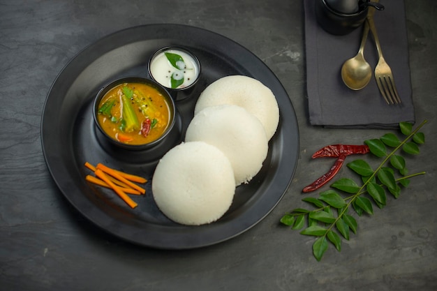Idly o Idli, artículo principal del desayuno del sur de la India, que está bellamente dispuesto en un plato negro con textura de color gris con fondo de cocina