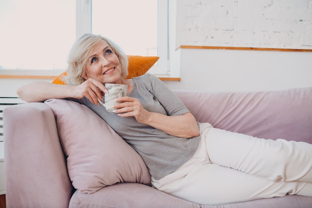 Idosa caucasiana idosa tomando chá da tarde e deitada no sofá em casa