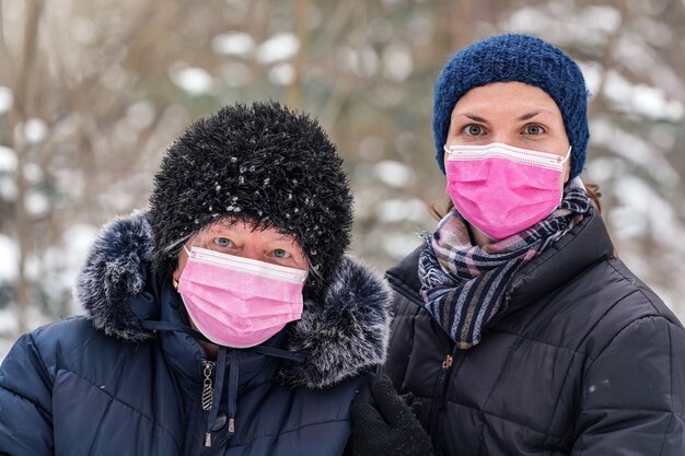 Idosa idosa com sua filha mais nova em roupas quentes de inverno, ambas usando máscara facial de vírus descartável rosa de uso único