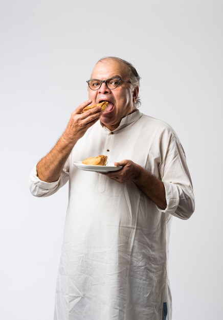 Idoso ou idoso indiano comendo samosa ou massa de vegetais
