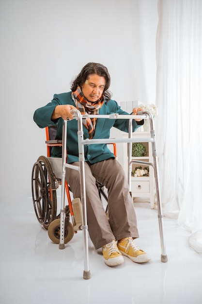 Idoso sentado em cadeira de rodas tentando andar com andador em cuidados domiciliares