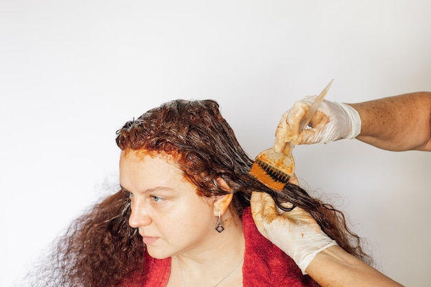 Idoso tingindo o cabelo feminino de cor vermelha com ajuda de pincel nas mãos em luvas de látex brancas sobre fundo branco Coloração de cabelo em casa Livrando-se de cabelos grisalhos Antiidade