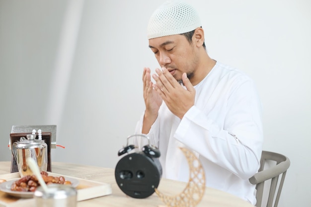 Iftar-Gericht mit muslimischer Hand, der zu Allah betet Datteln mit einem Glas heißem Tee auf dem Tisch