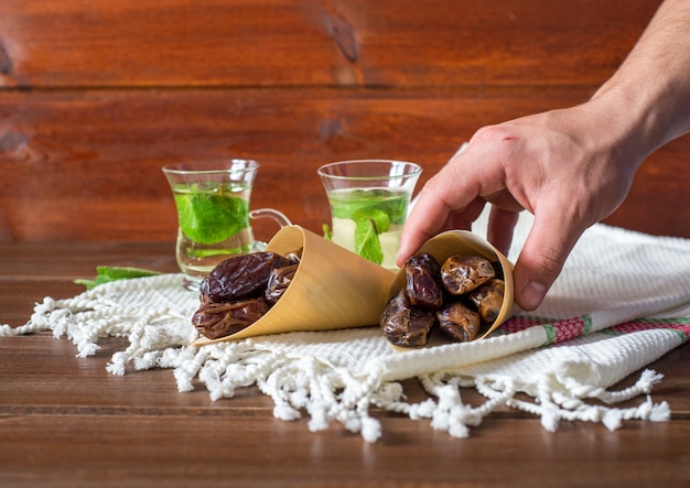 Iftar- oder Suhoor-Snack, Hand eines Mannes mit einem Konus von Daten mit Mentha-Tee, Ramadan-Konzept