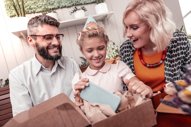 Igen moderno. garota simpática e positiva sorrindo enquanto recebe um presente caro dos pais