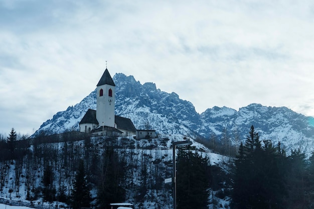 Iglesia y árboles en la montaña cubierta de nieve con el cielo de fondo