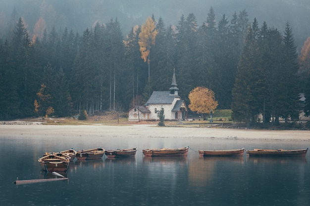 Iglesia y barcos de madera en Lago di Braies imagen cambiante tomada durante la lluvia en otoño, Dolomitas, Italia