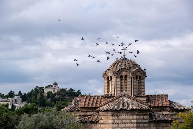 Iglesia ortodoxa griega en la zona de Thissio Atenas Grecia Bandada de palomas volando alrededor de la cúpula fondo de cielo nublado
