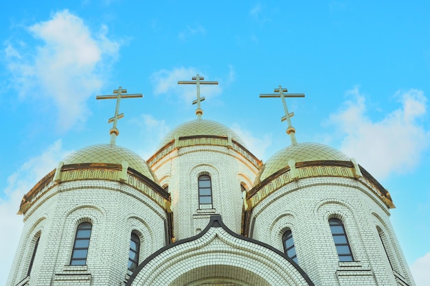 Iglesia ortodoxa de ladrillo con cúpulas doradas y 3 cruces contra el telón de fondo de un hermoso cielo nublado.