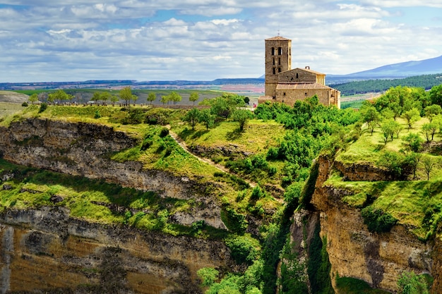 Igreja à beira do precipício em um campo verde com céu nublado. Sepulveda, Segovia, Espanha.