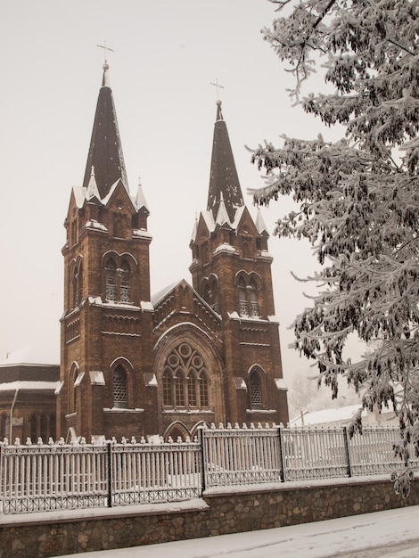 Igreja católica romana com cerca de ferro e árvores cobertas de neve no inverno