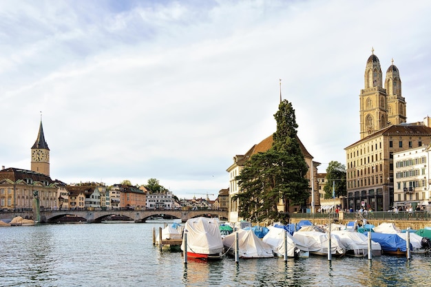 Igreja de São Pedro e Igreja Fraumunster, e barcos no cais do Rio Limmat, no centro da cidade de Zurique, Suíça. Pessoas no fundo