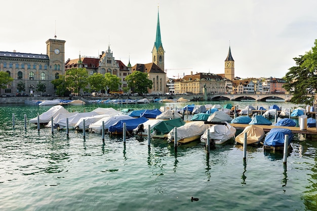 Igreja de São Pedro, Igreja Fraumunster e barcos no cais do Rio Limmat, no centro da cidade de Zurique, Suíça. Pessoas no fundo