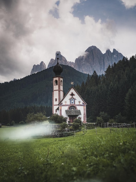 Igreja em campo gramado com montanhas em fundo contra o céu nublado