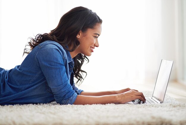 Ihren Status aktualisieren Aufnahme einer jungen Frau, die zu Hause auf ihrem Laptop im Internet surft