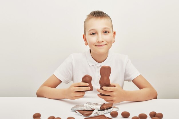 Ild¡Niño con conejitos de chocolate y huevos de pascua. Huevos de chocolate, conejos y azulejos. Dulces de chocolate para niños