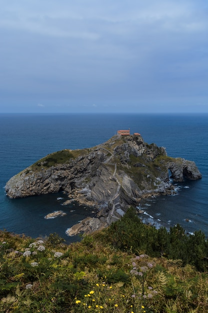 Ilha de Gaztelugatxe de folhagem e céu nublado