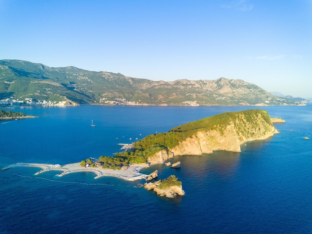 Ilha de São Nicolau com vegetação nas margens do mar Adriático contra o pano de fundo das cidades costeiras das montanhas montenegrinas e céu claro