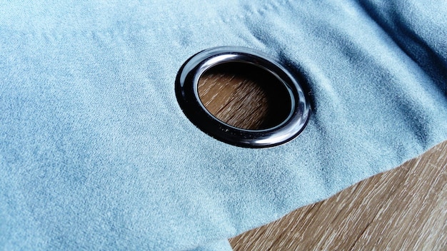 Ilhós de metal em uma cortina de veludo cinzaazul O tecido está em uma mesa de madeira Buraco no material