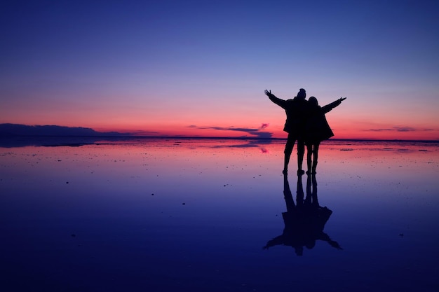 ilhouette de pareja feliz en la superficie de inundación del Salar de Uyuni en el cielo crepuscular Bolivia