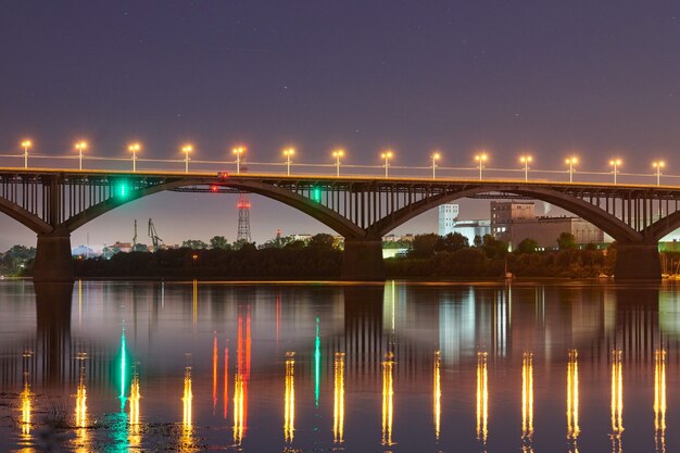 Iluminação da ponte da cidade à noite. Belo reflexo das luzes noturnas na superfície da água. Fotografia de longa exposição.