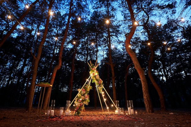 Iluminação de luzes de cordas festivas na decoração do arco boho tipi no local da cerimônia de casamento ao ar livre em pinho