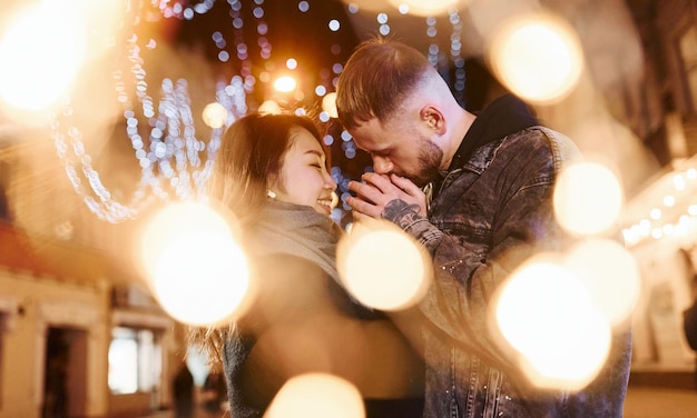 Iluminación artificial por guirnaldas Feliz pareja multirracial juntos al aire libre en la ciudad celebrando el Año Nuevo