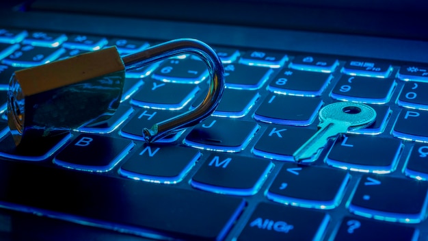 Iluminación azul del teclado del portátil con candado abierto y llave. Concepto de tecnología.