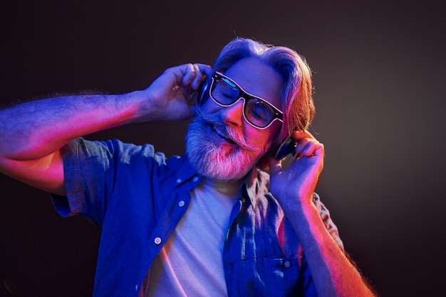 Iluminación de neón En los auriculares El hombre mayor moderno y elegante con cabello gris y barba está en el interior