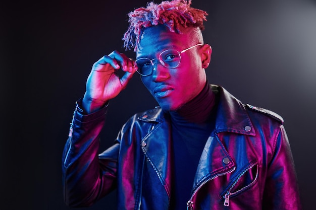 Iluminación de neón futurista Joven afroamericano con gafas de pie en el estudio