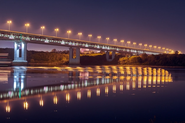 Iluminación del puente de la ciudad de noche. Hermoso reflejo de luces nocturnas en la superficie del agua