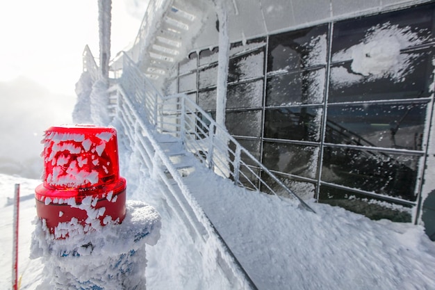 Iluminación roja de emergencia con escaleras y ventanas cubiertas de nieve y hielo en la cima de la estación de esquí de Chopok, que ilustra el frío extremo en invierno. Jasna, Eslovaquia.