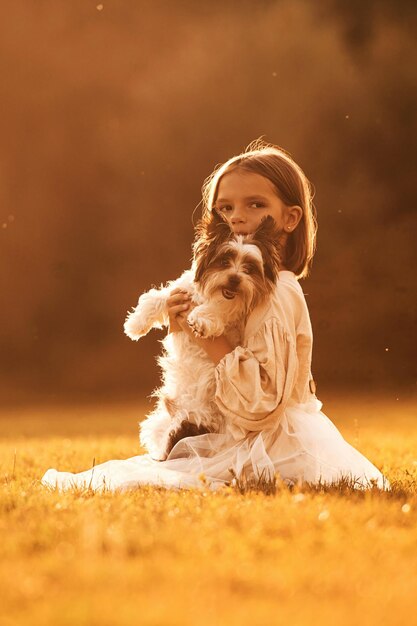 Foto iluminada por la luz del sol una niña linda está en el campo con un perro