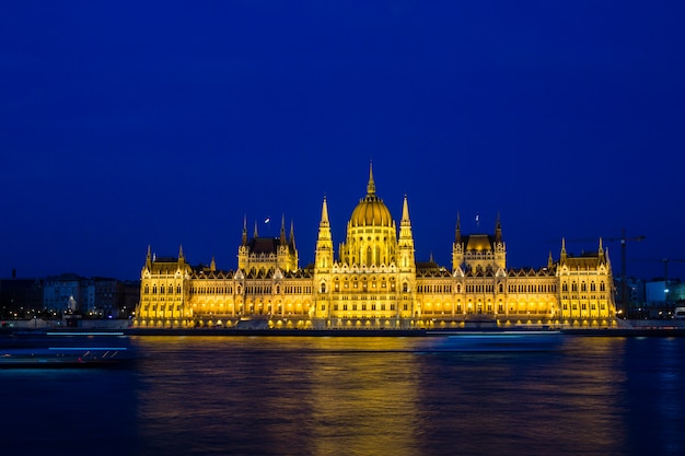Iluminado o edifício do parlamento de budapeste à noite com céu escuro e reflexão no rio danúbio