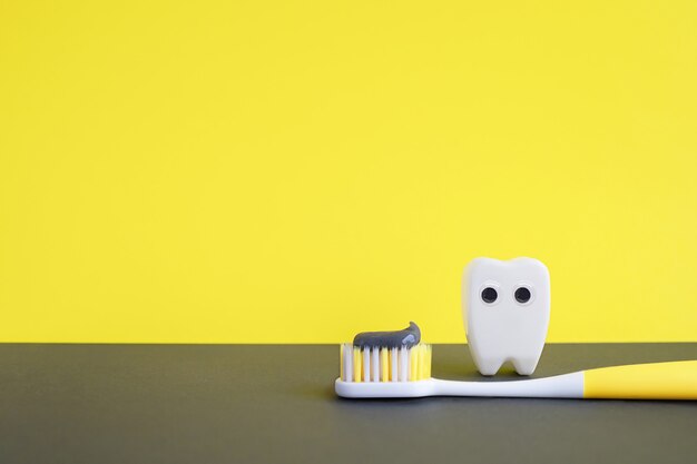 Iluminando a escova de dentes amarela com pasta de dente e dente de brinquedo branco no fundo cinza final. conceito de odontologia.